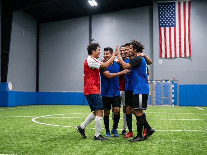 Adult players celebrating a goal with high-fives on the indoor field